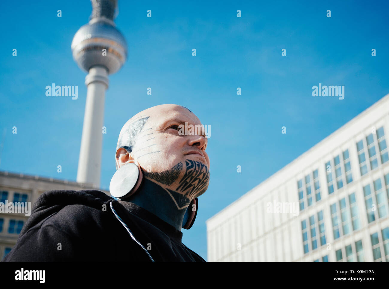 Low Angle Sicht des Menschen mit Tätowierungen und Ohrenstöpsel unter dem Fernsehturm, Berlin, Deutschland Stockfoto