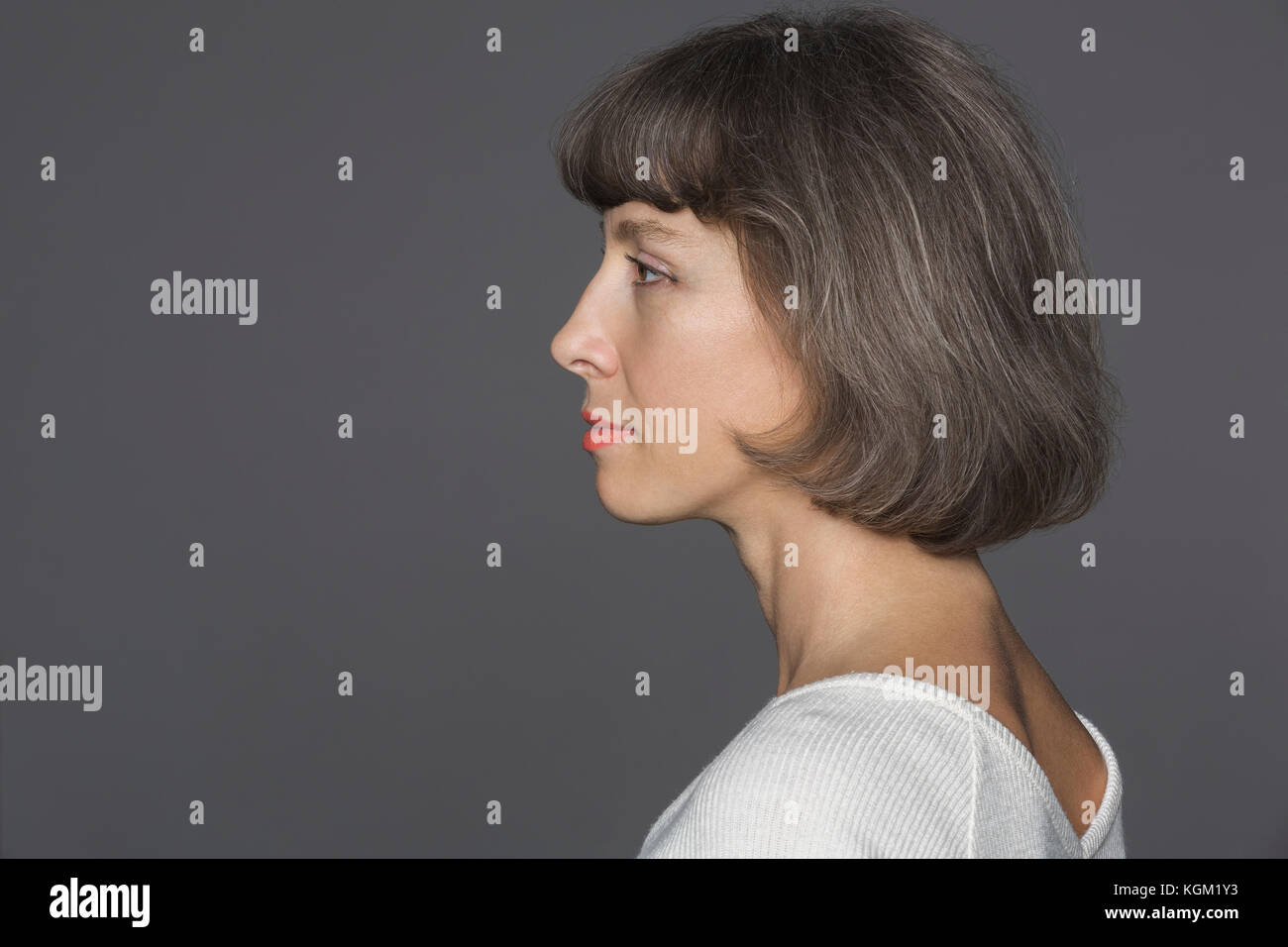 Seitenansicht der reifen Frau mit braunen Haaren gegen grauer Hintergrund Stockfoto