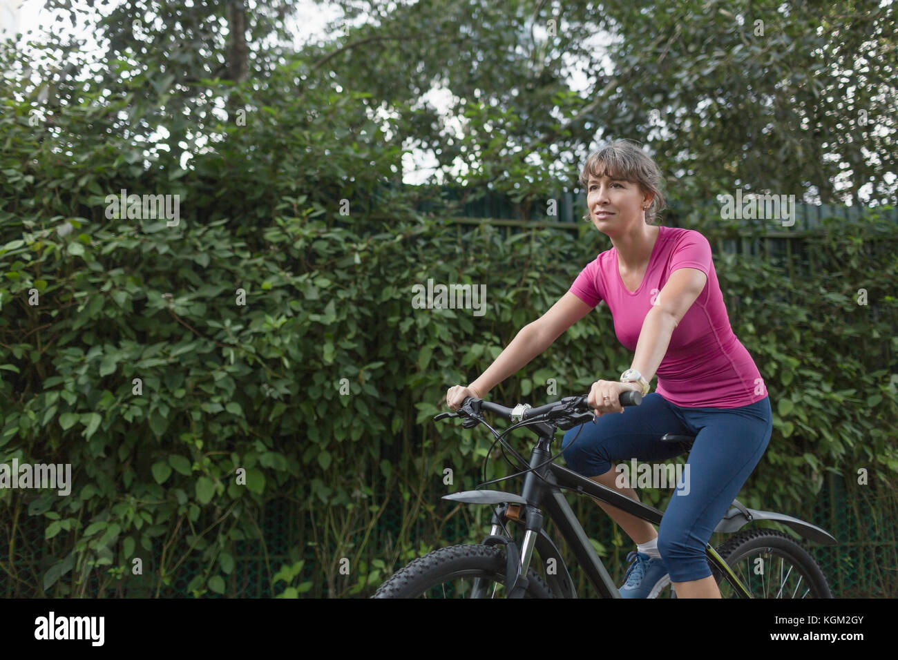 Volle Länge des Frau Reiten Fahrrad von Pflanzen Stockfoto