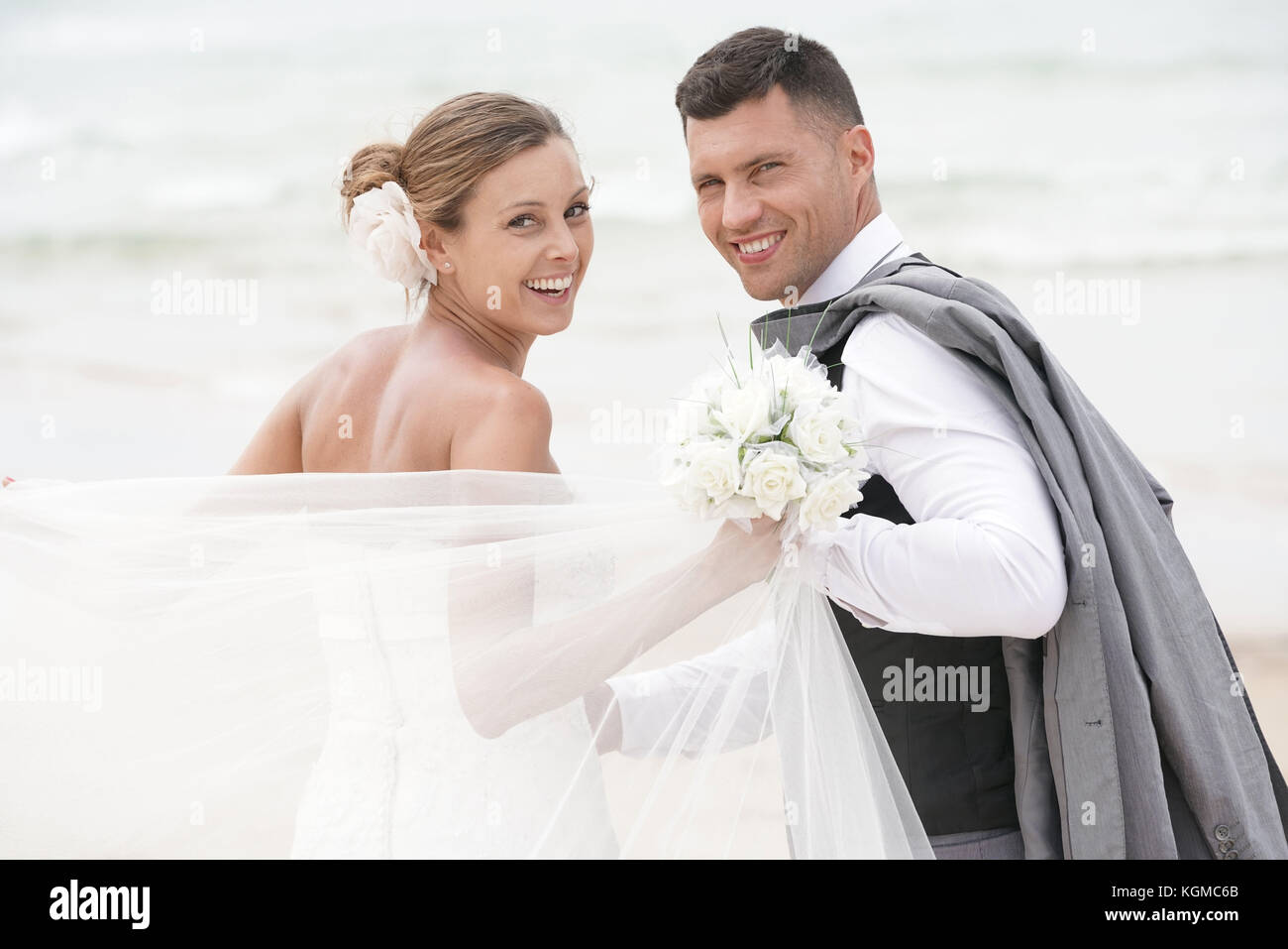 Fröhlich frisch verheiratete Ehepaar zu Fuß am Strand Stockfoto