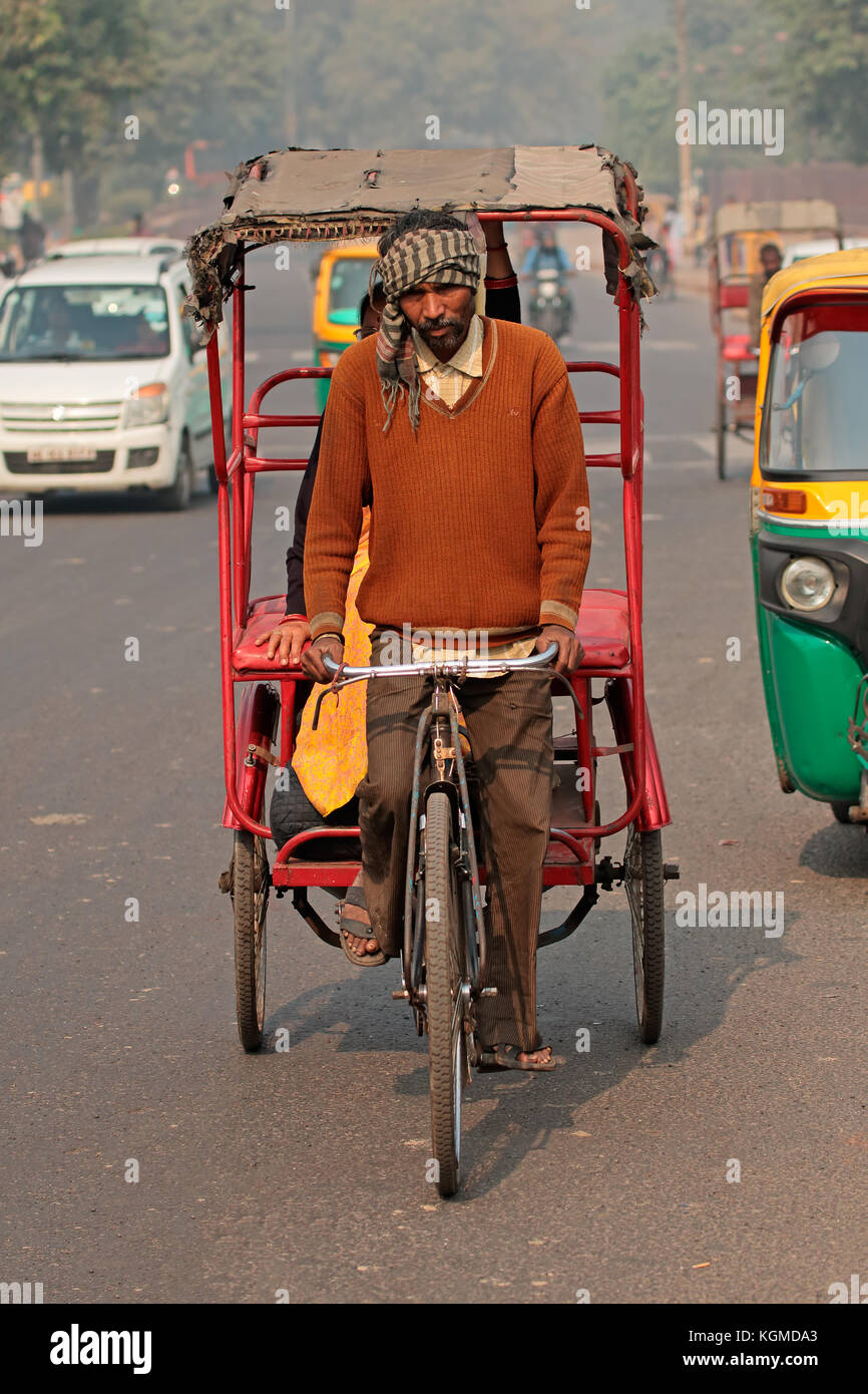 Delhi, Indien - 20. November 2015: Zyklus Rikscha Fahrer Transporte ein Passagier in der überfüllten Verkehr mit sichtbaren smog Luftverschmutzung Stockfoto