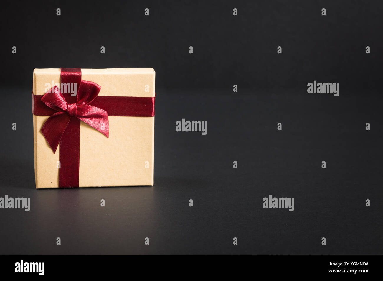 Papier Geschenkkarton mit Deep red ribbon und einen Bogen, auf schwarzem Hintergrund. Stockfoto