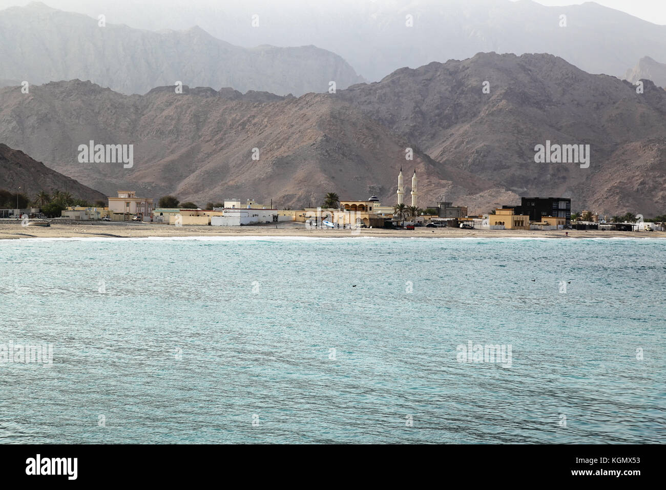 Blick auf einen leeren Strand in Oman mit Moschee und traditioneller arabischer Architektur, al Hajar Berge im Hintergrund Stockfoto