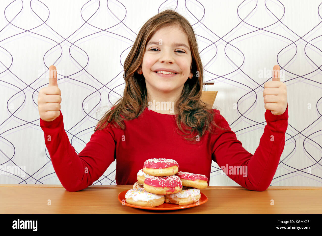 Glückliche kleine Mädchen mit Donuts und Daumen hoch Stockfoto