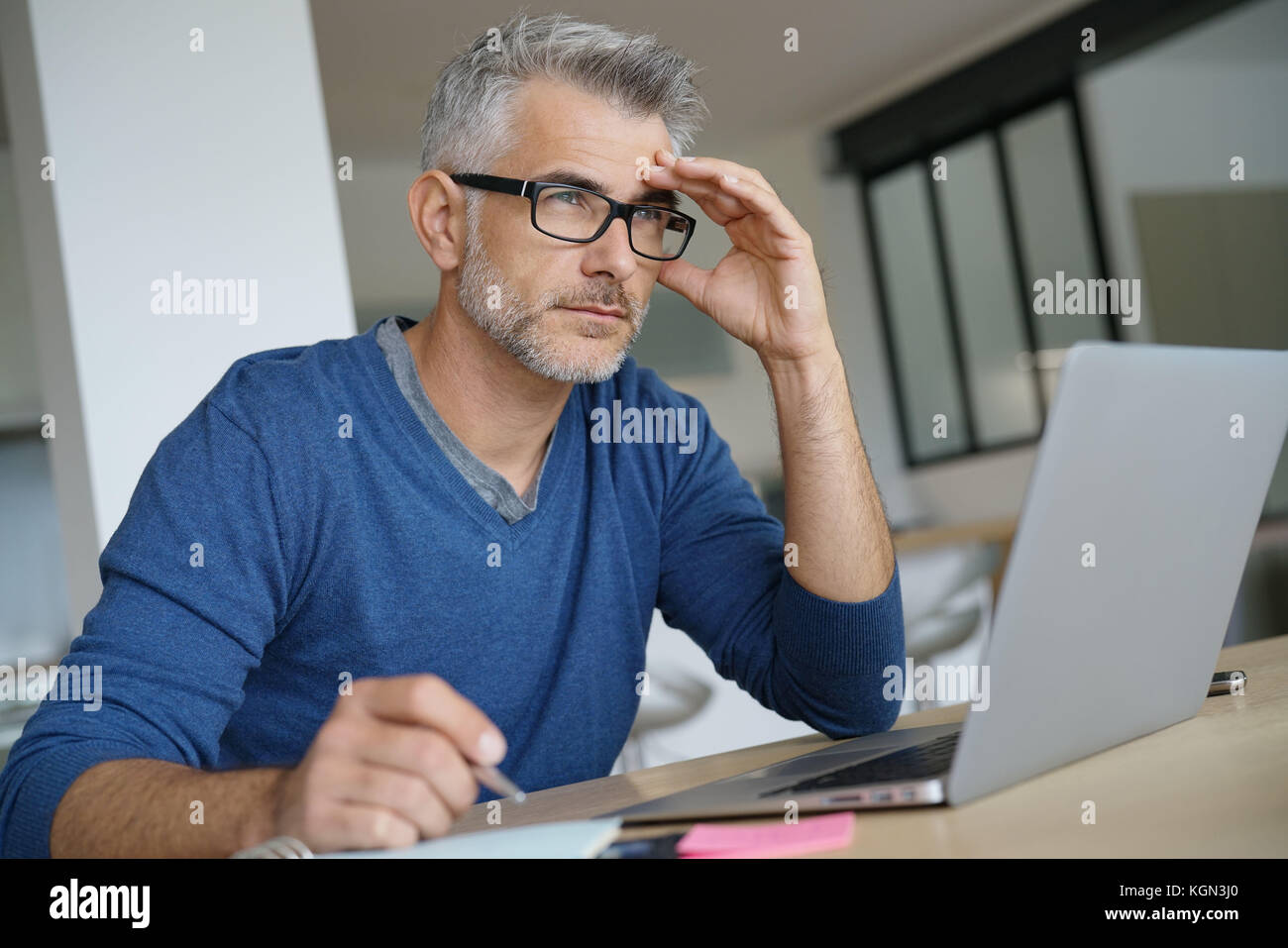 Mann mittleren Alters Arbeiten am Laptop-nachdenklichen Blick Stockfoto