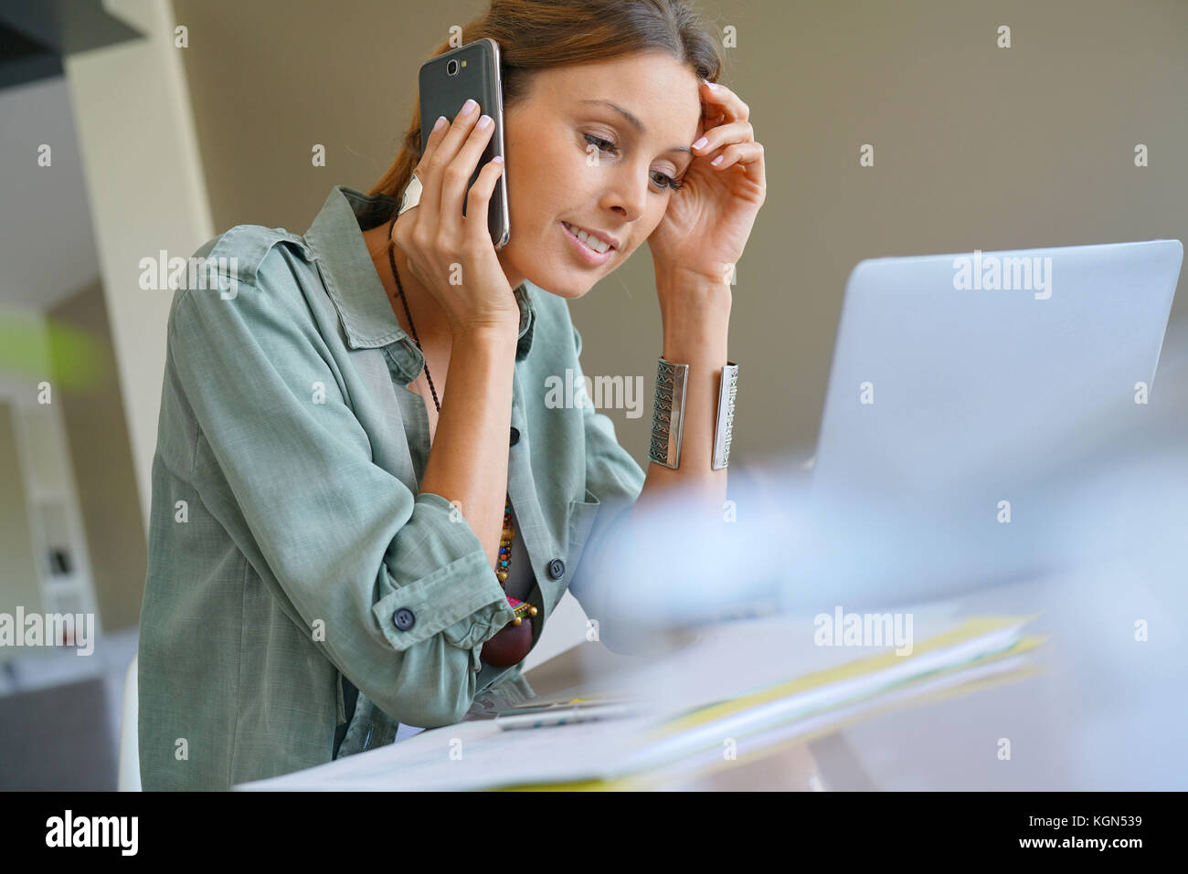 Frau von zu Hause aus arbeiten am Laptop und am Telefon sprechen Stockfoto