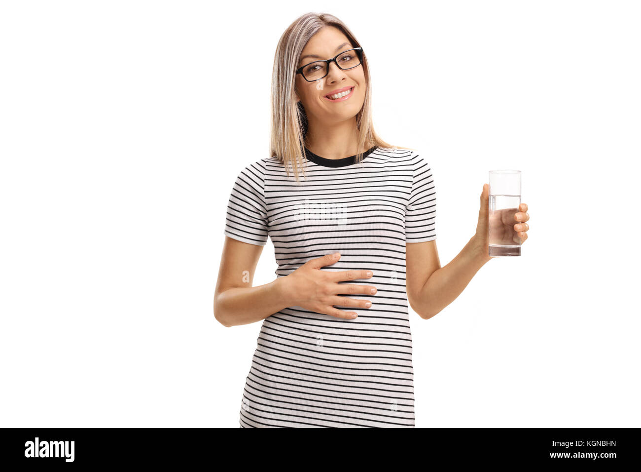 Zufriedene junge Frau mit einem Glas Wasser ihre Hand auf ihren Bauch auf weißem Hintergrund Stockfoto