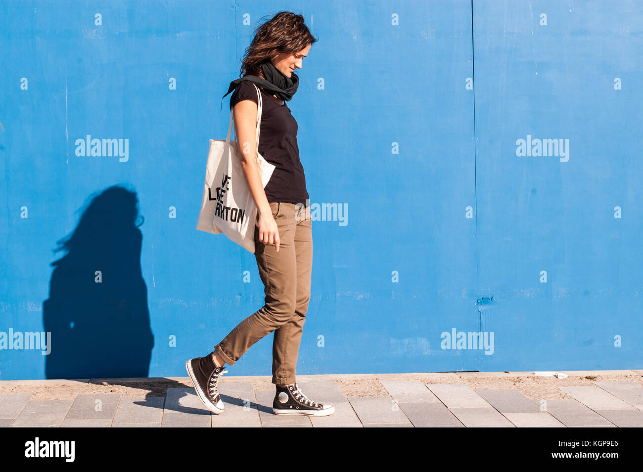 Junge Mädchen in casual braun Chinos, schwarze Turnschuhe und T-Shirt zu  Fuß auf einer Straße mit blauen Wand im Hintergrund gekleidet  Stockfotografie - Alamy