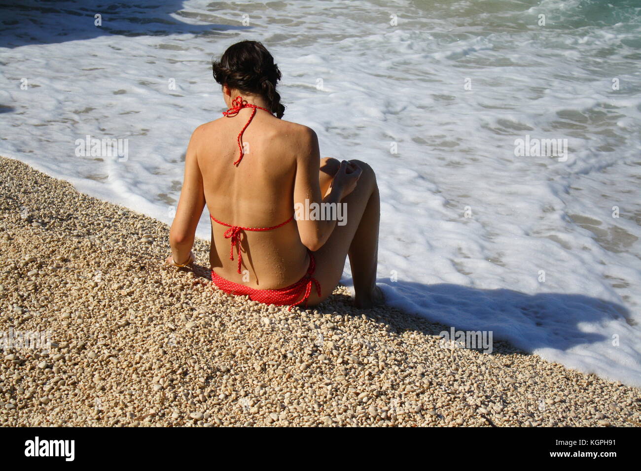 Eine Frau in einem roten Bikini sitzen und entspannen am Strand in Sardinien, Italien Stockfoto