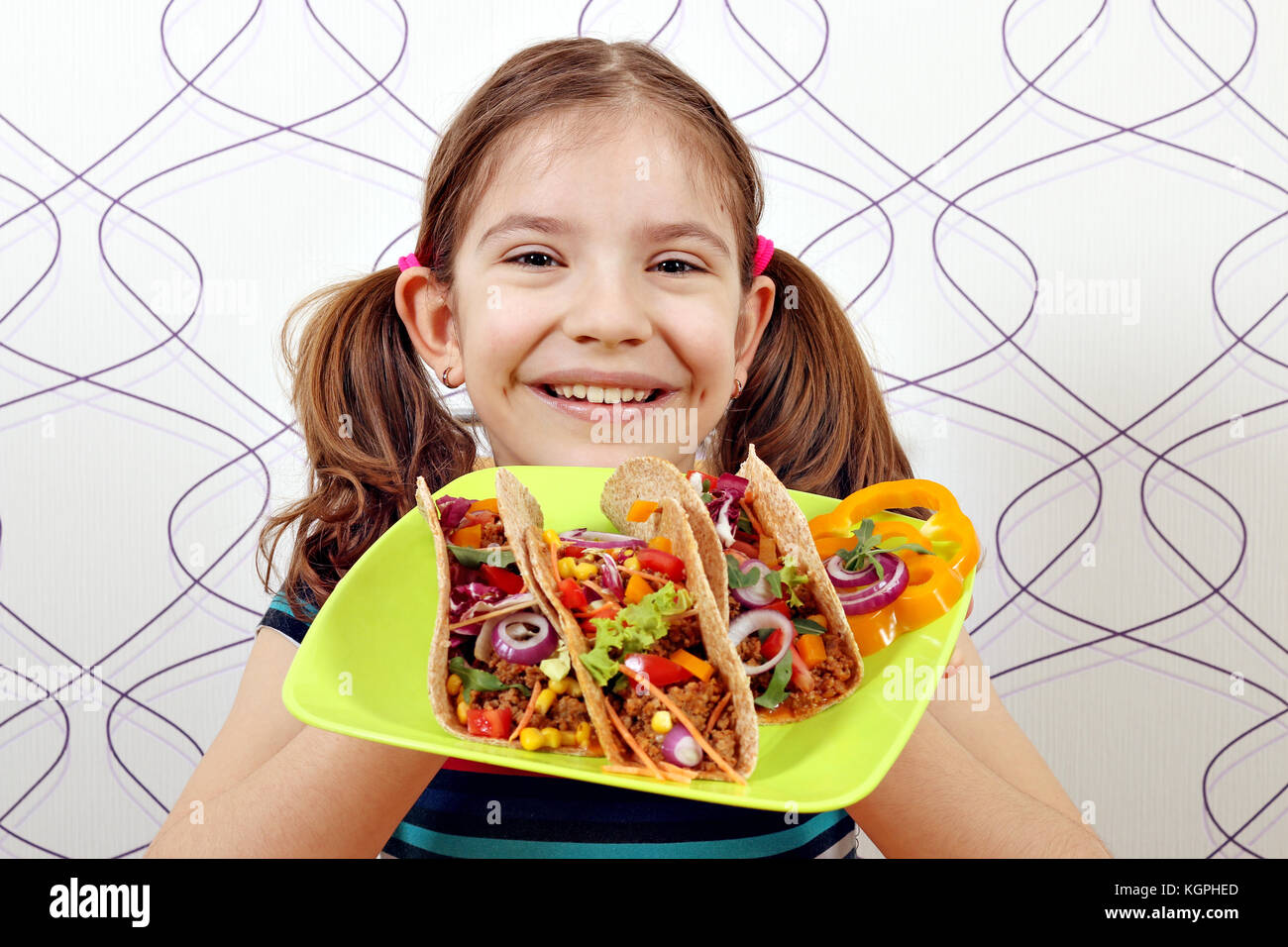 Glückliche kleine Mädchen mit Tacos auf Platte Stockfoto