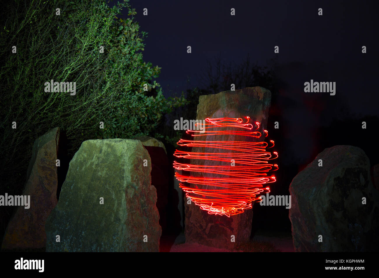 Helle Malerei, Lichtkunstfotografie: Rote Orebe schwicht im Freien mitten in der Luft zwischen alten Steinen im Dunkeln. Unheimliche, mysteriöse Nachtszene. Stockfoto