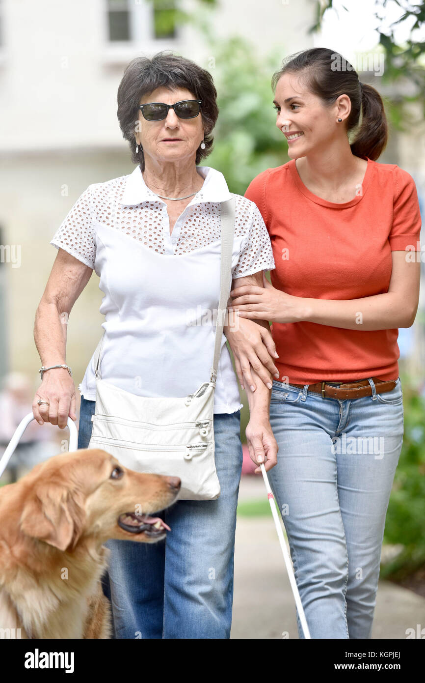 Ältere blinde Frau gehen mit Hilfe von Hund und Pflegeperson Stockfoto
