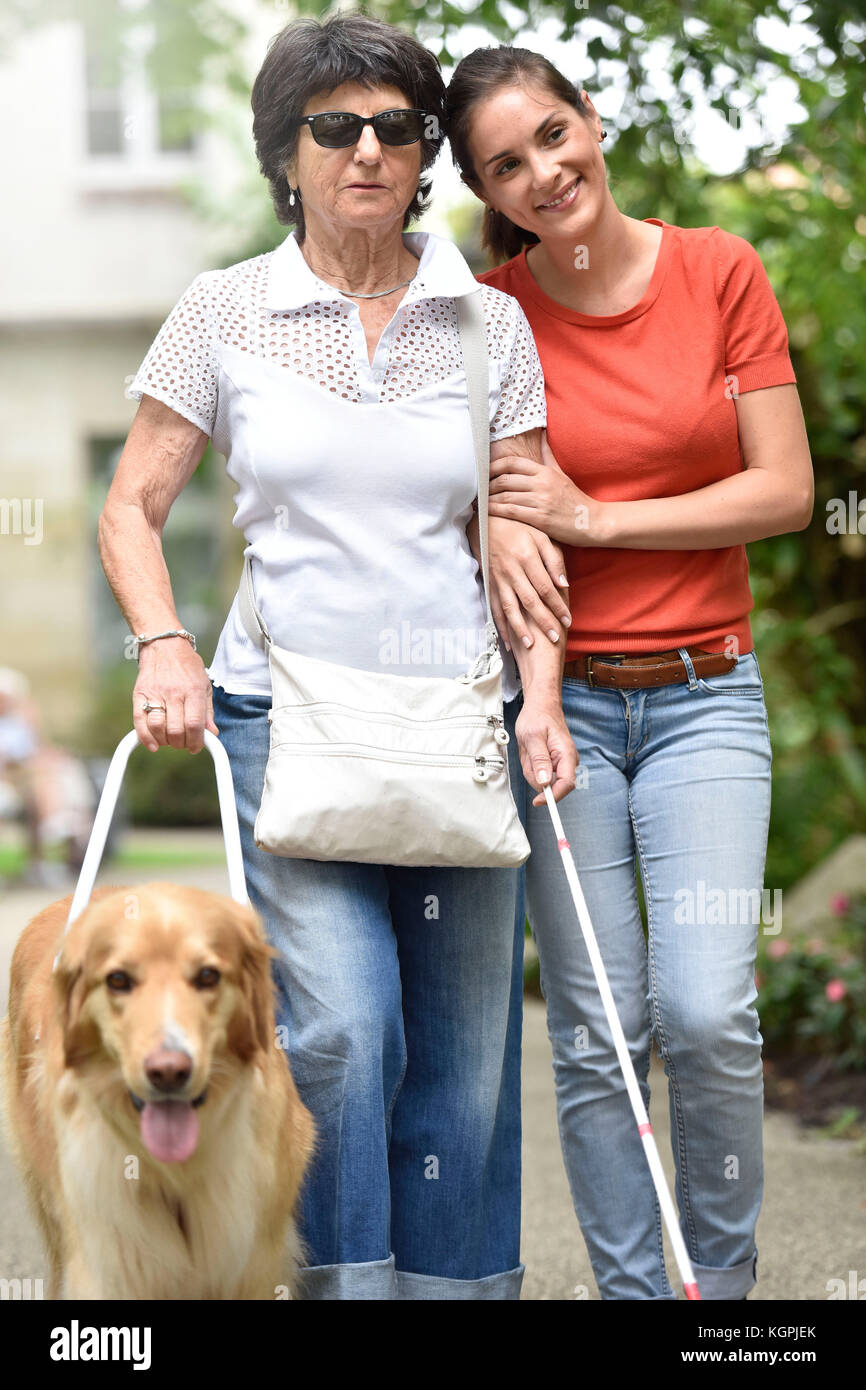 Ältere blinde Frau gehen mit Hilfe von Hund und Pflegeperson Stockfoto