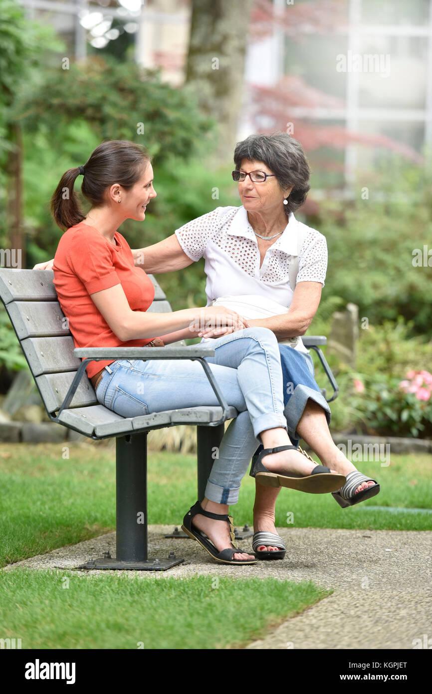 Ältere Frau mit pflegeperson sitzt auf der Bank im Park Stockfoto