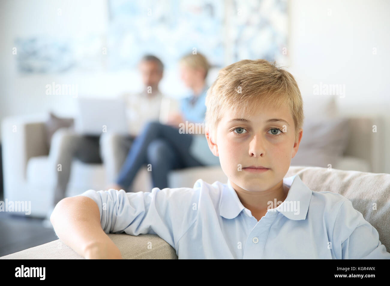 Der 12-jährige Jungen in die Couch zu Hause sitzen, Eltern im Hintergrund Stockfoto