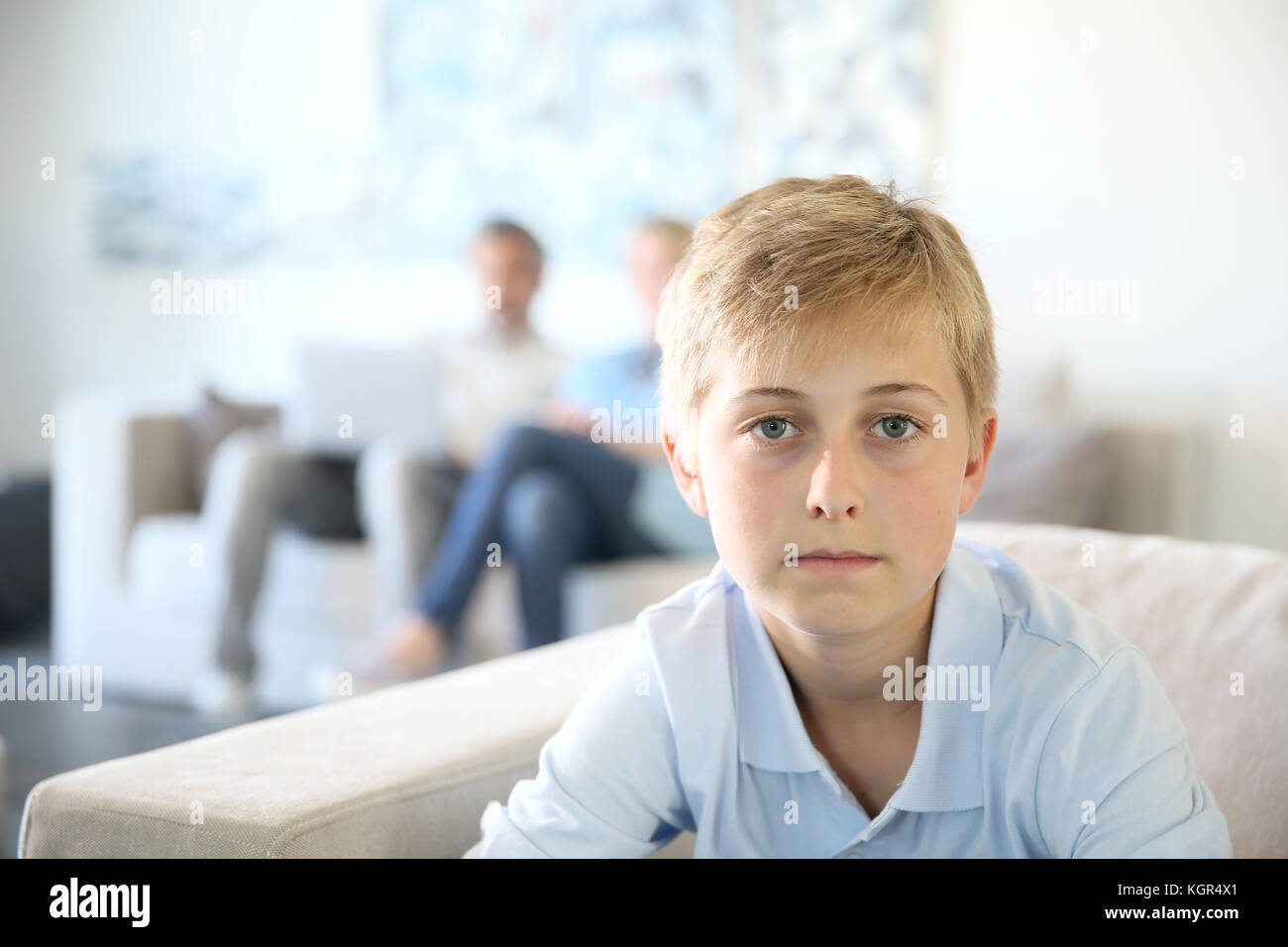 Der 12-jährige Jungen in die Couch zu Hause sitzen, Eltern im Hintergrund Stockfoto