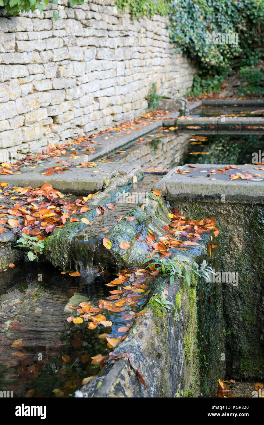 Stein Wasser Rinnen im Herbst Blätter in Bisley, Cotswolds, Gloucestershire, England abgedeckt Stockfoto