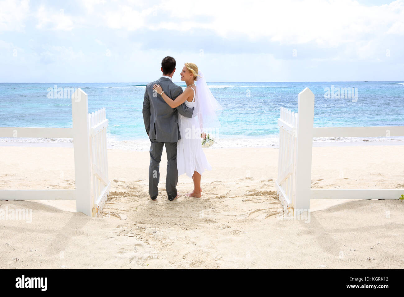 Frisch verheiratete Ehepaar stehend durch einen Zaun zu diesem Ozean Stockfoto