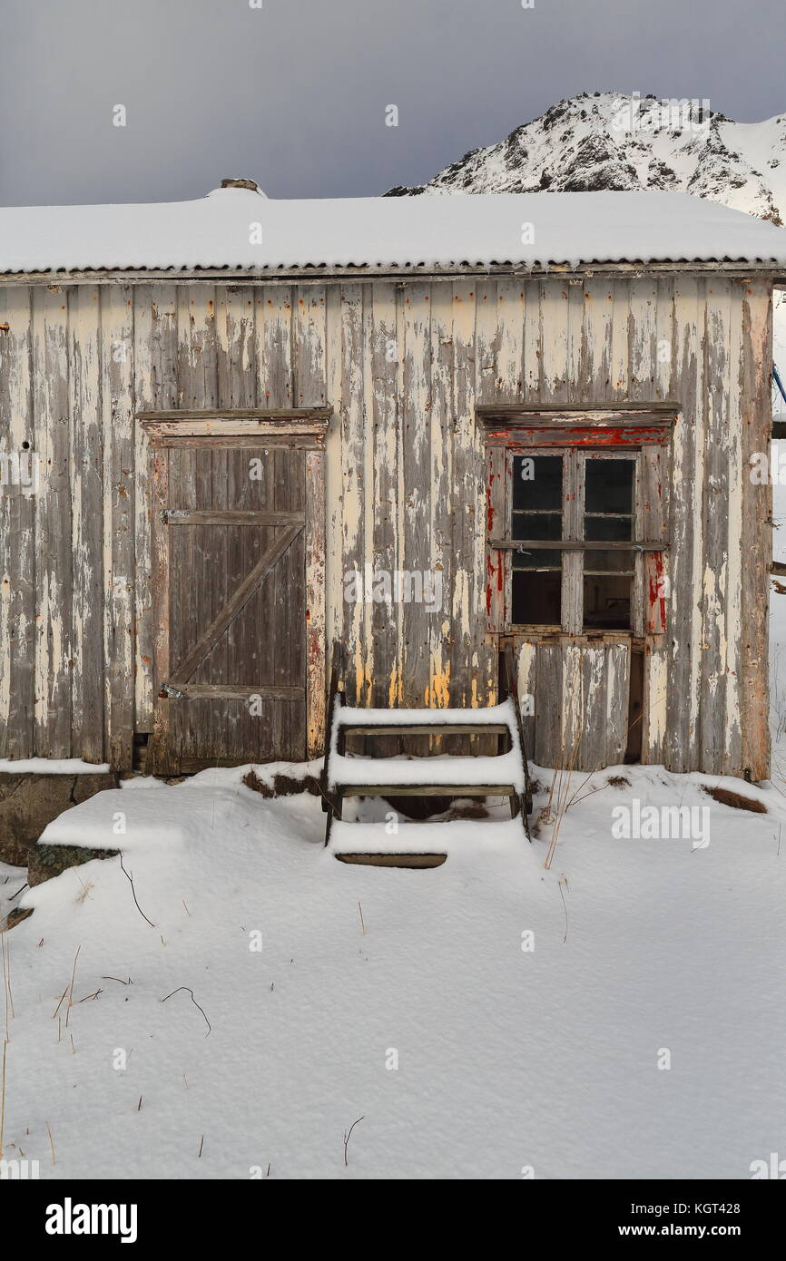 Schnee bedeckt völlig ruiniert - verlassen - Farbe verblasst Holzhütte mit Treppe lehnte sich an der Wand - Fuß des schneebedeckten hustinden neben e10 European Road Mount Stockfoto