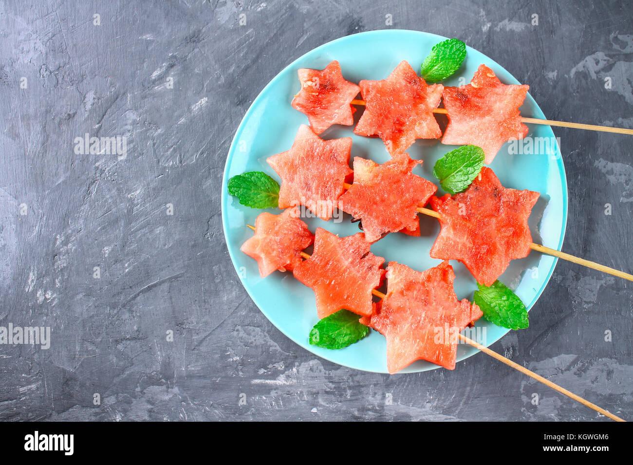 Wassermelone in Form von Sternen auf Spieße mit Blättern der Minze liegt auf einer Platte. Die blaue Teller ist wie eine Rakete im Weltraum. top View Stockfoto