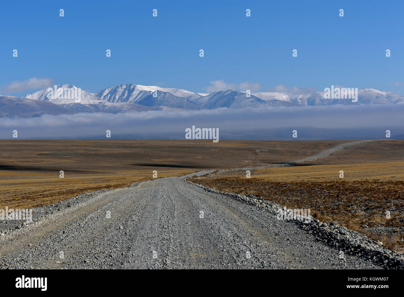 Landschaftlich reizvolle Steppenlandschaft mit einer Schotterstraße in der Steppe, Berge mit Schnee und der Tubulären Cloud auf dem Hintergrund des blauen Himmels und schöne überdachte Stockfoto