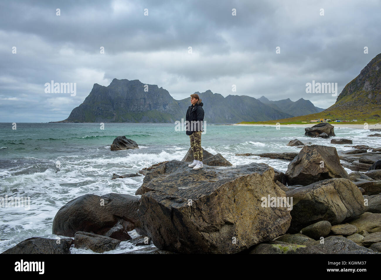 Boy steht auf einem großen Felsen und geniesst die Aussicht über einen Strand in Norwegen Stockfoto