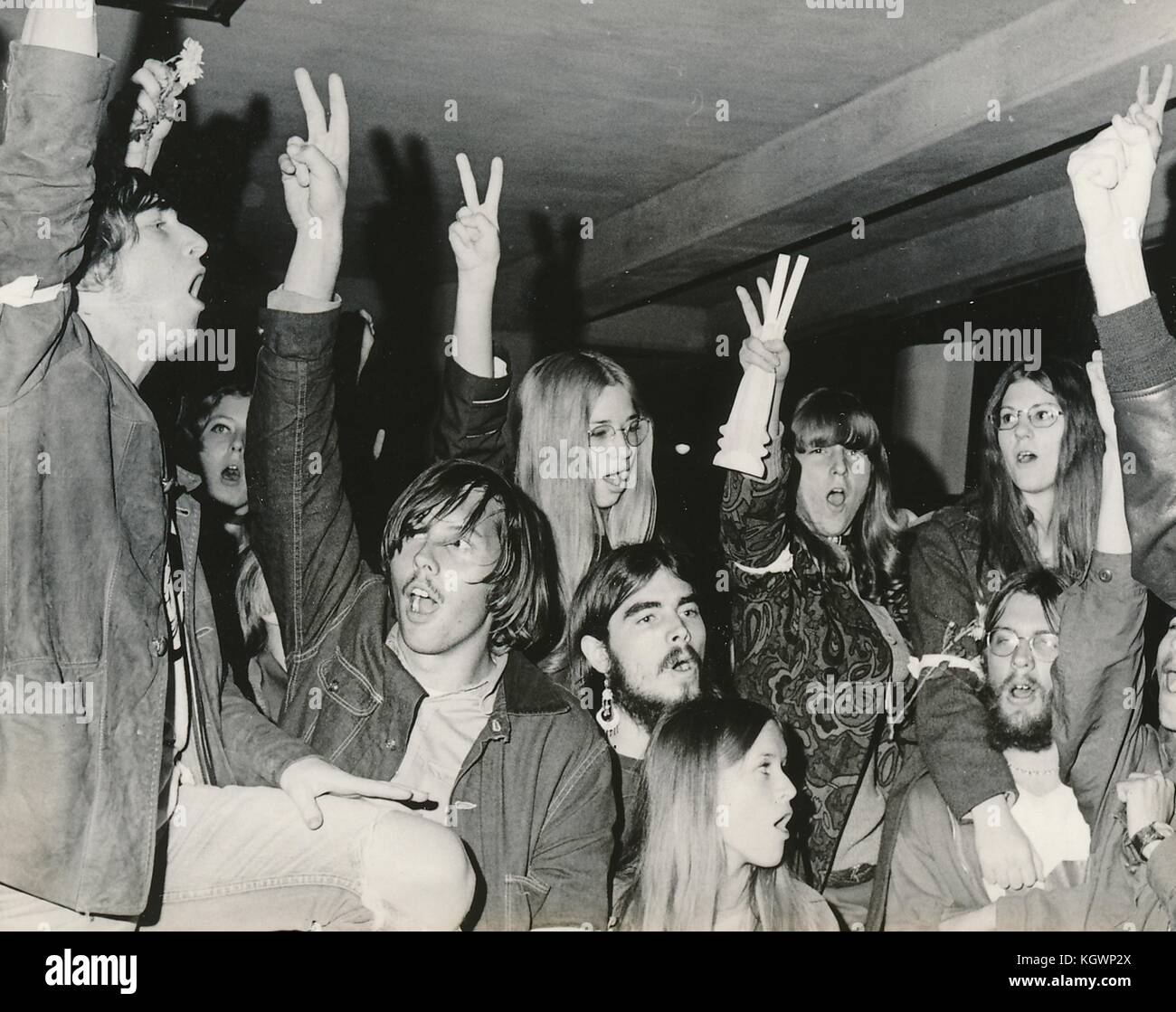 Eine große Gruppe von Studenten in Hippie-Kleidung, einschließlich psychedelisch gemusterter Kleidung, Anti-Kriegs-Armbänder und langes Haar, halten ihre Finger in einer Friedenszeichen-Geste hoch, während eines Studentenprotests gegen den Vietnamkrieg an der North Carolina State University, Raleigh, North Carolina, mit einigen Studenten, die in der Höhe Blumen in ihren Armbändern hielten und Blumen in ihren Armbändern trugen, 1970. () Stockfoto