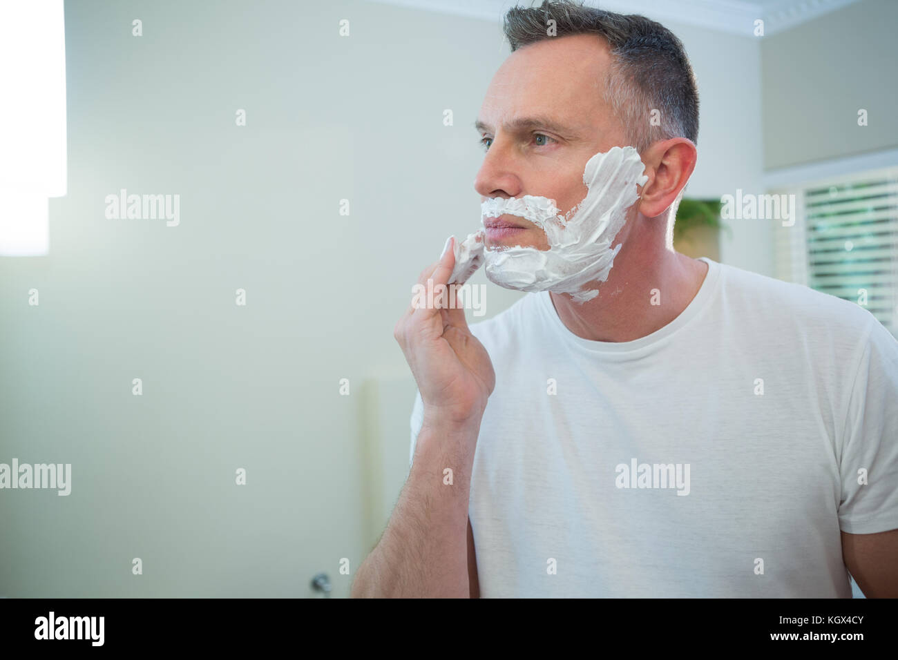 Mann Anwendung Rasierschaum auf seinem Gesicht im Badezimmer Stockfoto