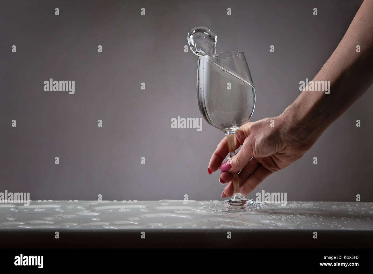 In der Nähe der weiblichen Hand mit einem Glas Wein mit Wasser gefüllt, auf nassen Tisch Stockfoto