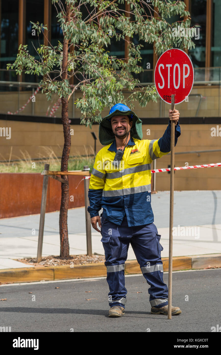 Sydney, Australien - 25. März 2017: Lächelnder Bauarbeiter in voller gelber und blauer Schutzkleidung, der den Verkehr mit einem roten Stoppschild steuert Stockfoto