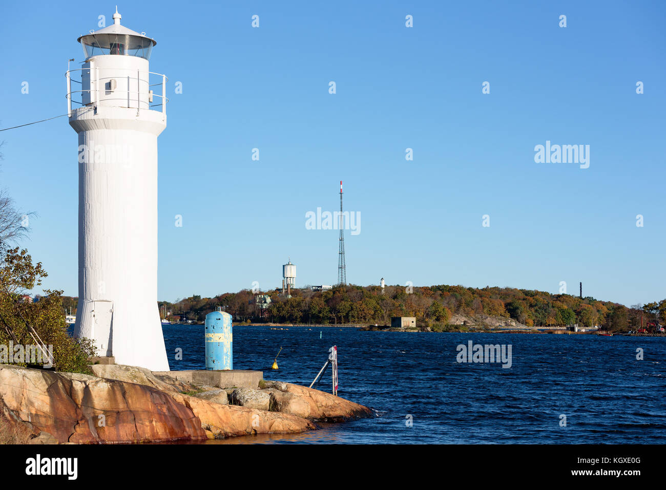 Kleinen weißen Leuchtturm auf der karlskrona (Schweden) Archipel Insel stumholmen mit Küstenlandschaft im Hintergrund. Wasserturm und Radio Antenne Stockfoto