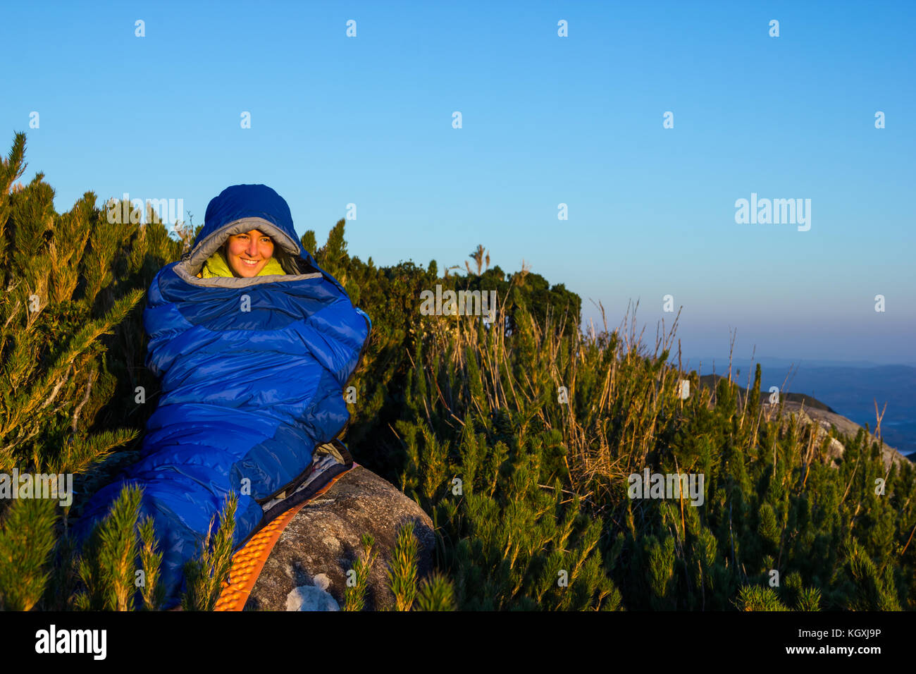 Junge Frau lächelnd innen blau Schlafsack auf der Spitze eines Berges Stockfoto