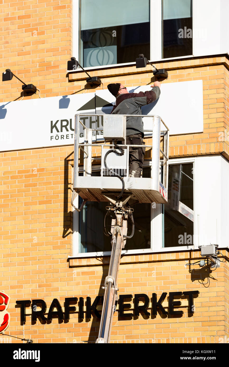 Karlskrona, Schweden - 30. Oktober 2017: Dokumentation des Alltags und der Umwelt. Arbeiter in der Hubarbeitsbühne, der ein Schild am Hochhaus anbringt Stockfoto