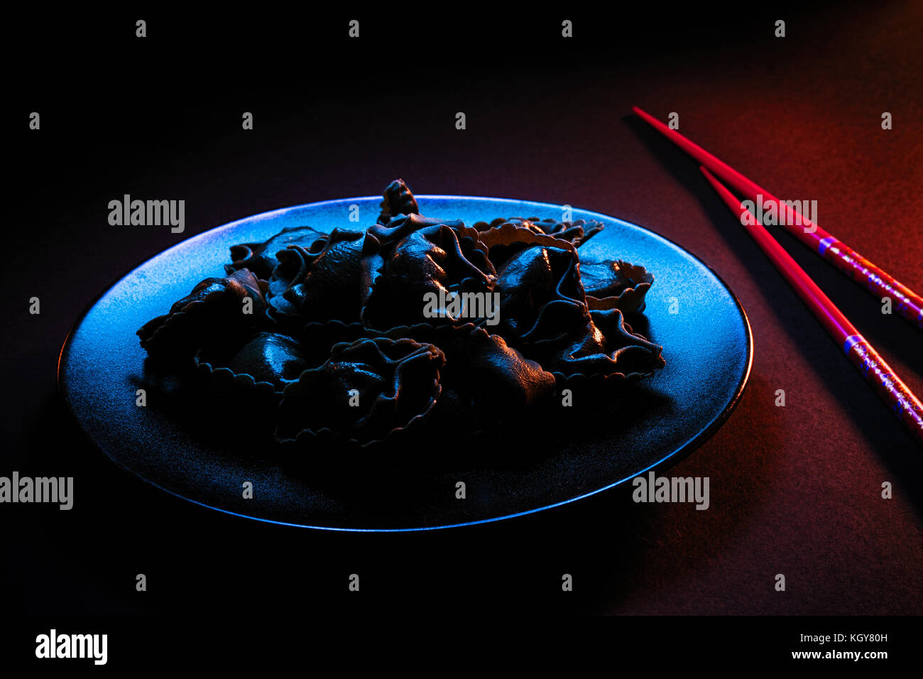 Platte des Schwarzen Knödel, auf eine schwarze Platte mit Paar rote Stäbchen, mit blauem Licht von TV-Bildschirm leuchtet Stockfoto