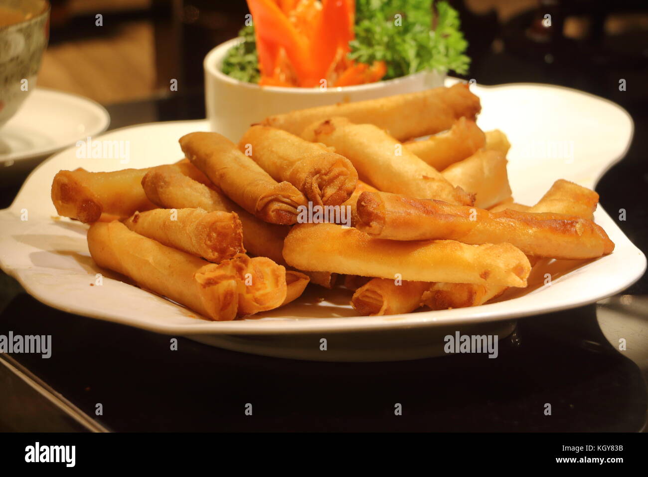 Asiatische Frühlingsrolle mit Käse oder gemahlenem Fleisch im Inneren und in Öl auf einem weißen Teller gebraten mit Salatgarnitur in einem Restaurant angezeigt. Stockfoto