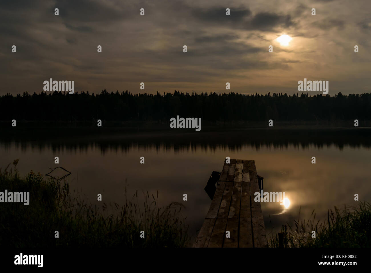 Nacht Landschaft mit Mond, Wolken, Wald, Reflexionen und Moonlight auf der glatten Wasser des Sees Stockfoto