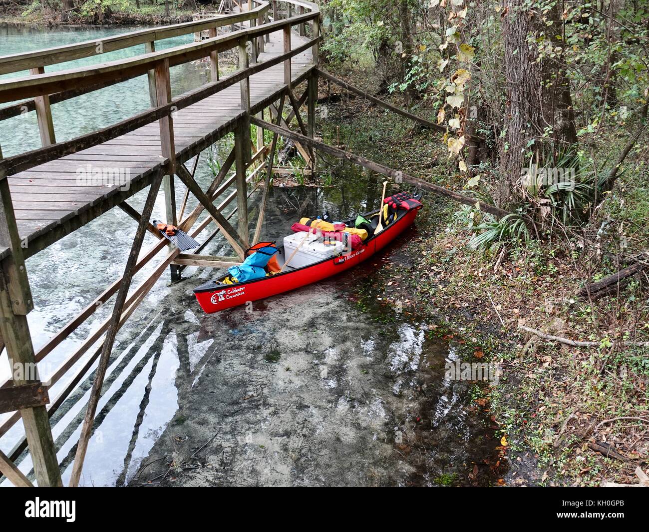 Kanu mit Campingausrüstung, unter Holzsteg während Paddler (unsichtbar) Frühstück am Ufer. Gilchrist Blue Springs State Park, Florida, USA. Stockfoto