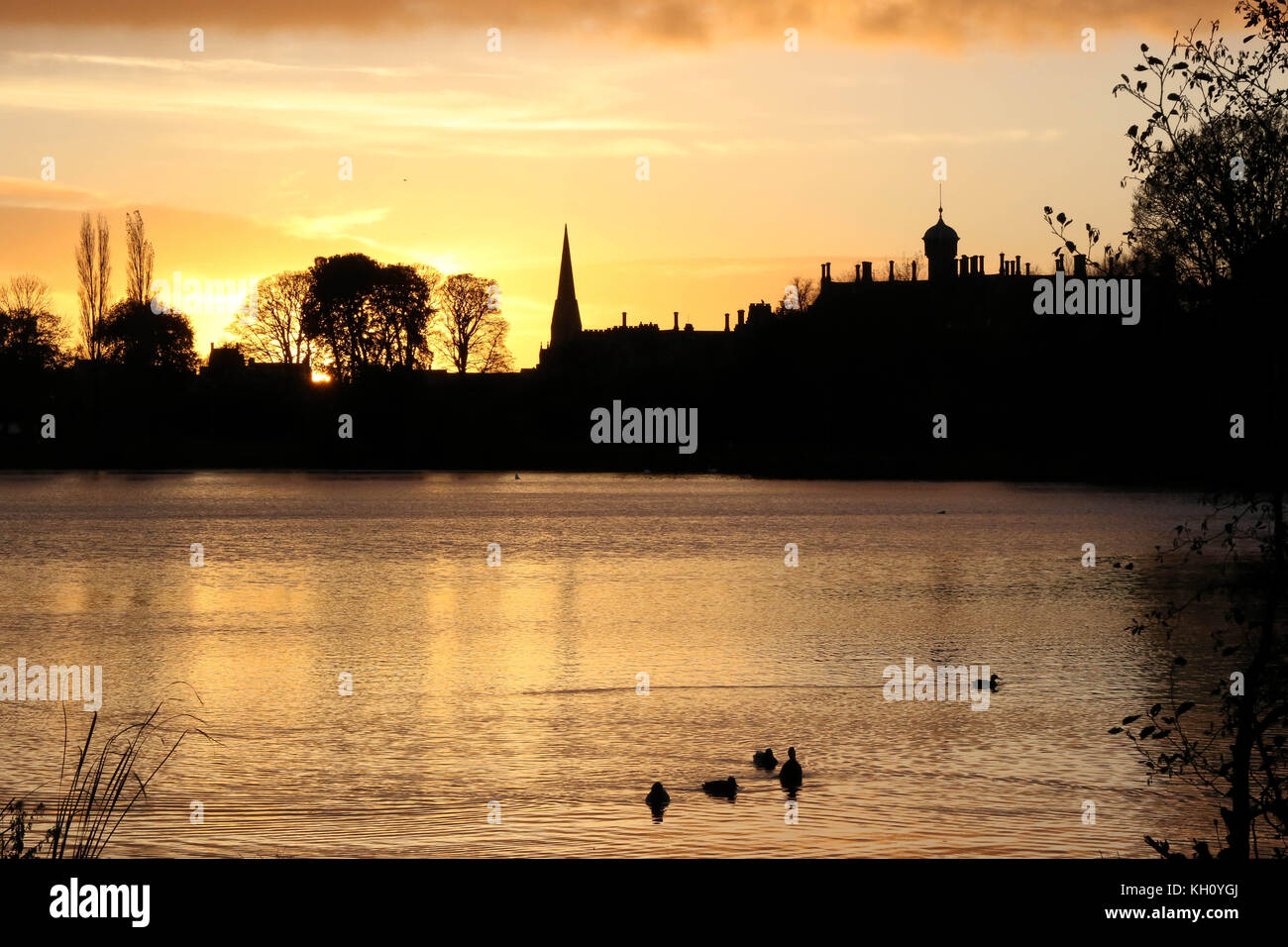 Lurgan Park See, Nordirland, Großbritannien. 12. November 2017. Ein blustery Tag mit kalten Nord-westlichen Winden und Duschen endet mit Clearing Skies und fallende Temperaturen. Frost zu rechnen ist, möglicherweise als niedrig zu-4C in ländlichen Gebieten, wie die Sonne auf der linken Seite von Shankill Pfarrkirche und Brownlow House (rechts). Quelle: David Hunter/Alamy Leben Nachrichten. Stockfoto