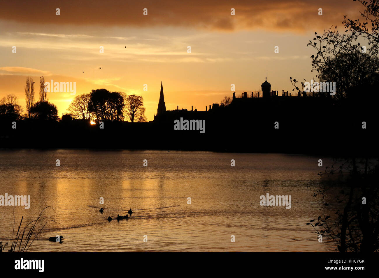 Lurgan Park See, Nordirland, Großbritannien. 12. November 2017. Ein blustery Tag mit kalten Nord-westlichen Winden und Duschen endet mit Clearing Skies und fallende Temperaturen. Frost zu rechnen ist, möglicherweise als niedrig zu-4C in ländlichen Gebieten, wie die Sonne auf der linken Seite von Shankill Pfarrkirche und Brownlow House (rechts). Quelle: David Hunter/Alamy Leben Nachrichten. Stockfoto