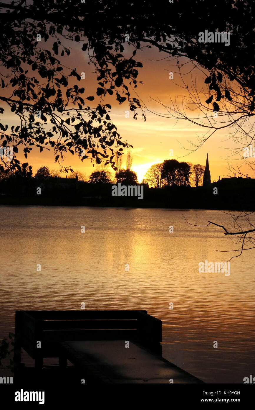 Lurgan Park See, Nordirland, Großbritannien. 12. November 2017. Ein blustery Tag mit kalten Nord-westlichen Winden und Duschen endet mit Clearing Skies und fallende Temperaturen. Frost zu rechnen ist, möglicherweise als niedrig zu-4C in ländlichen Gebieten, wie die Sonne auf der linken Seite von Shankill Pfarrkirche und Brownlow House (rechts). Quelle: David Hunter/Alamy Leben Nachrichten. Stockfoto