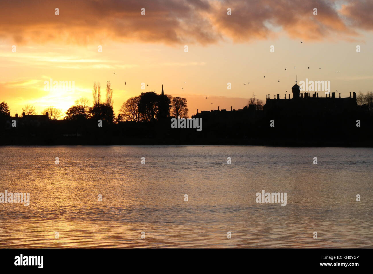 Lurgan Park See, Nordirland, Großbritannien. 12. November 2017. Ein blustery Tag mit kalten Nord-westlichen Winden und Duschen endet mit Clearing Skies und fallende Temperaturen. Frost zu rechnen ist, möglicherweise als niedrig zu-4C in ländlichen Gebieten, wie die Sonne auf der linken Seite von Shankill Pfarrkirche und Brownlow House (rechts). Quelle: David Hunter/Alamy Leben Nachrichten. Stockfoto