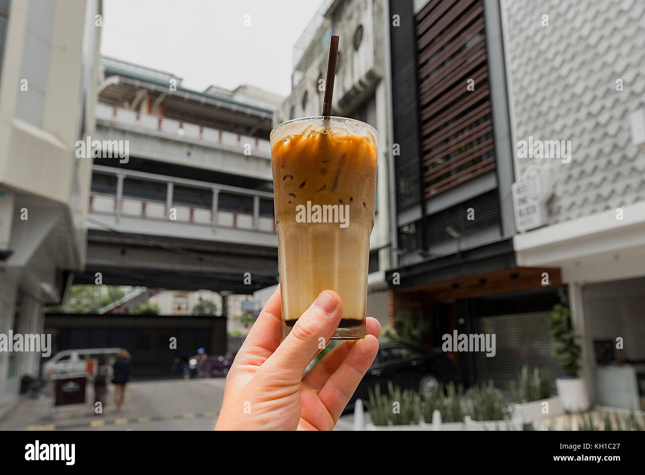 Eine menschliche Hand mit einem frisch zubereiteten Glas thai Eiskaffee in Bangkok Seitenstraße. Stockfoto