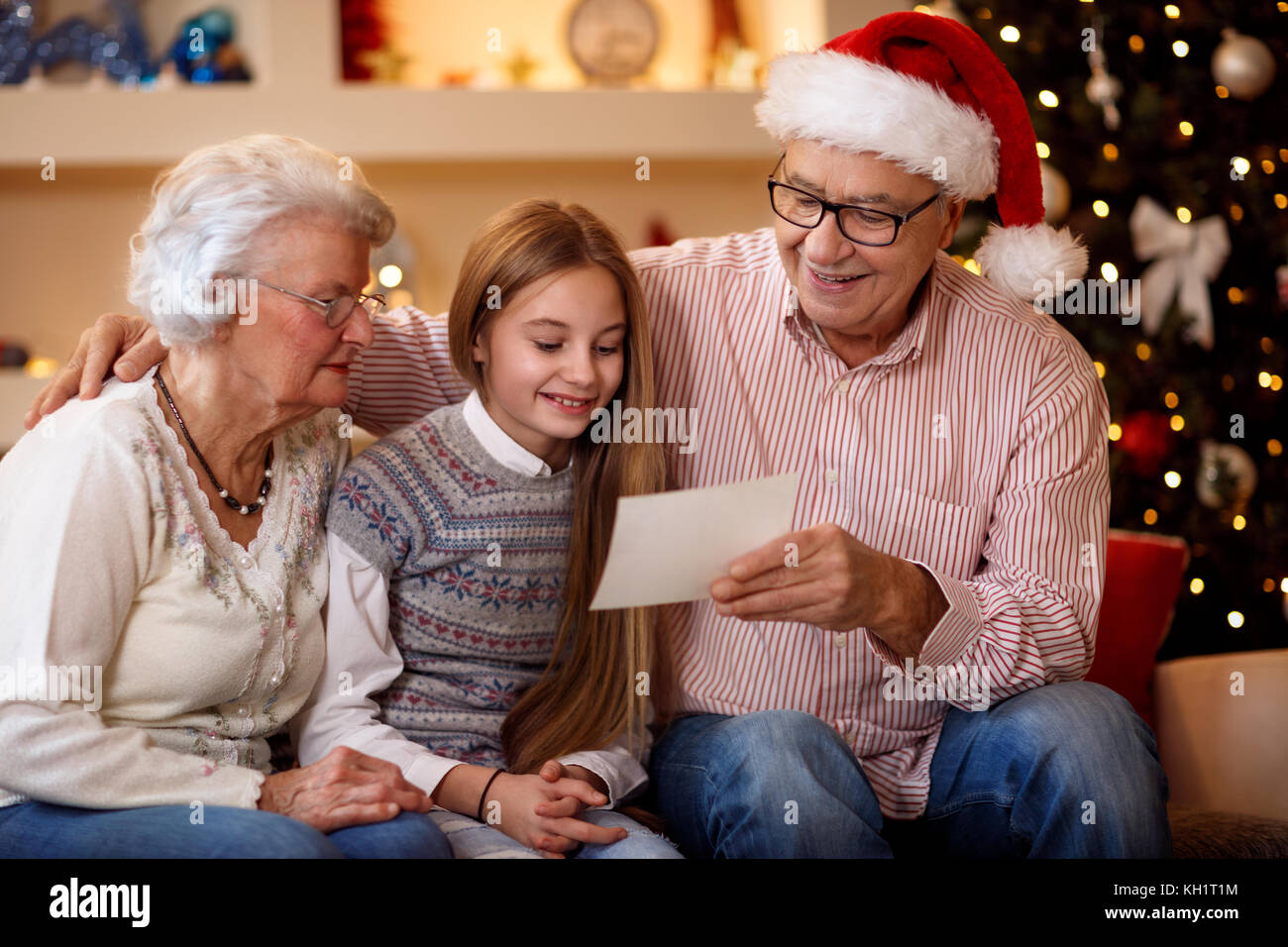 Lächelnd Großeltern mit Enkelin aufpassen Foto und teilen sich den Speicher am Heiligabend Stockfoto