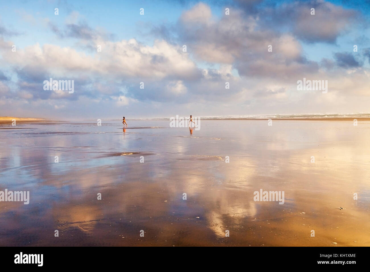 Junge Paare, die bei Sonnenuntergang über Ninety Mile Beach, Northland, Neuseeland, laufen. Stockfoto