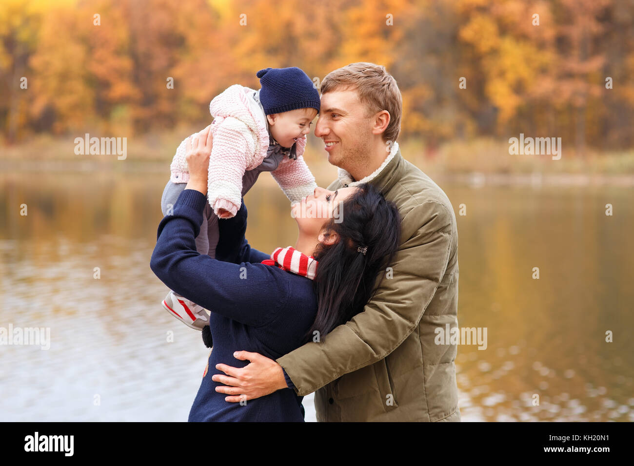 Junge Eltern spielen mit kleinen Tochter im Herbst Park in der Nähe des Sees. mom Holding Baby Mädchen in Händen. glückliche Familie, elterliche Liebe, Herbst Jahreszeit conce Stockfoto