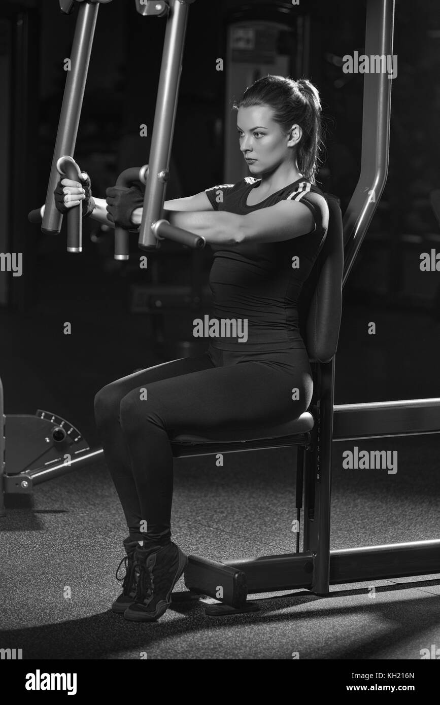 Frau am Sport Fitnessraum tun Arme übungen auf einer Maschine. Dunkle Sport Club. Schwarz und Weiß. Stockfoto