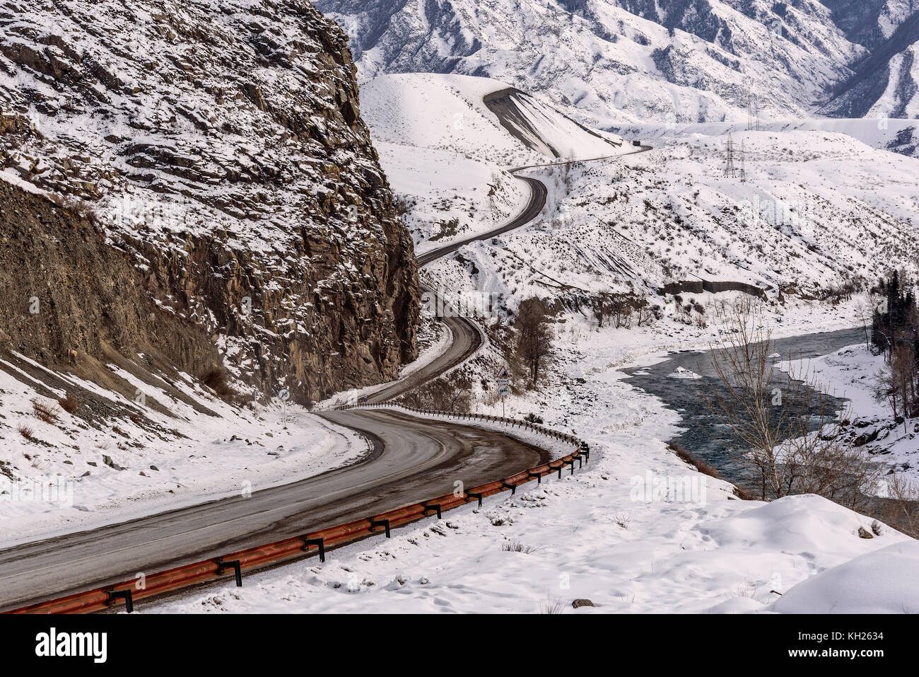 Malerische winter Blick mit dem gewundenen Asphaltstraße, Fluss und Bäume auf einem Hintergrund der Berge mit Schnee bedeckt Stockfoto