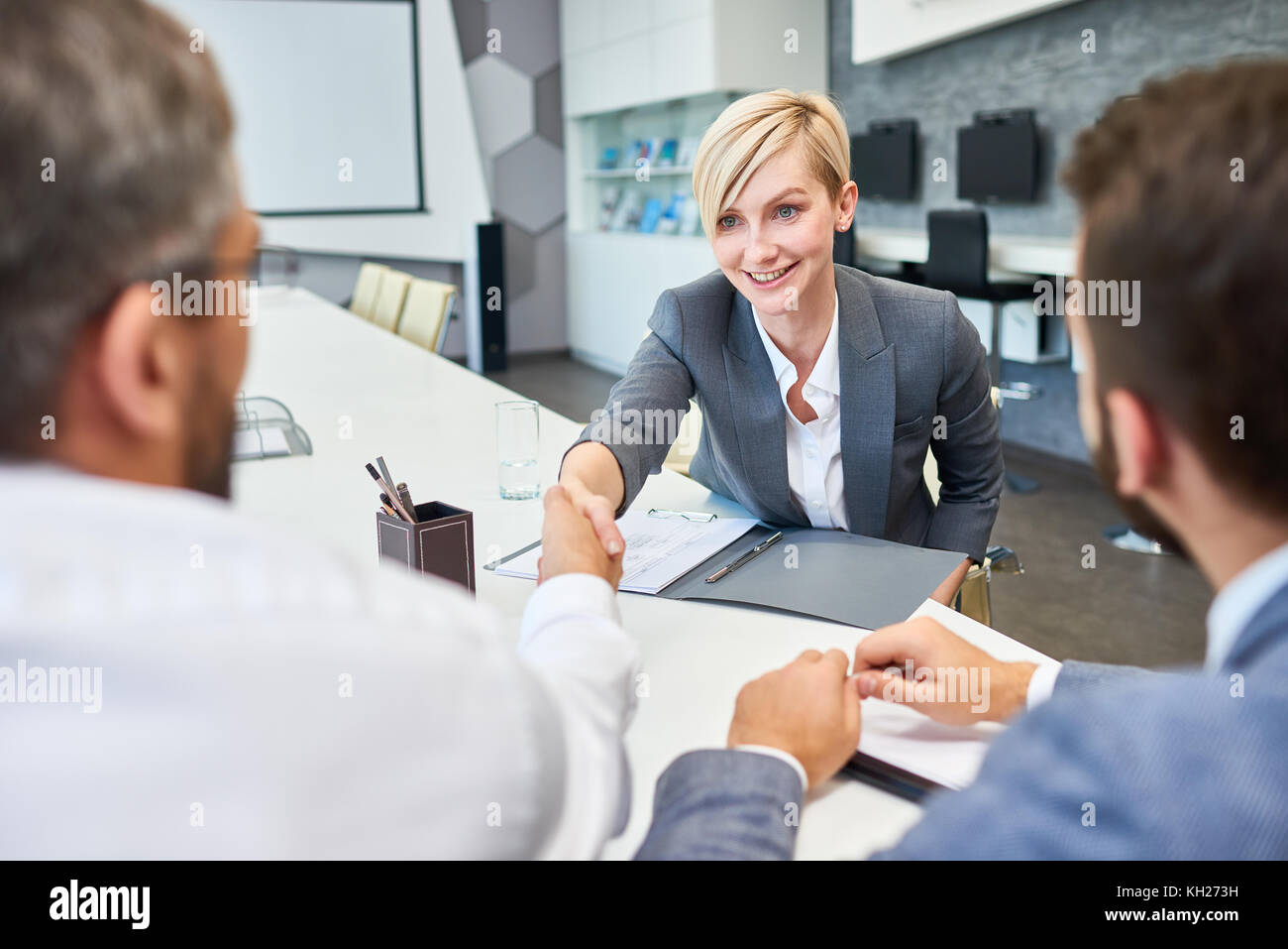 Portrait der Junge erfolgreiche Geschäftsfrau Händeschütteln mit Partnern in der Sitzung Tabelle im Board Room nach erfolgreicher Deal Stockfoto