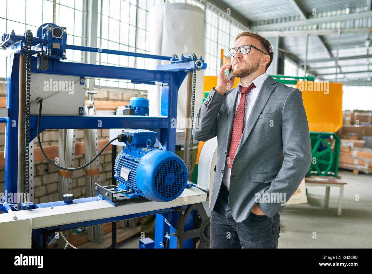 Porträt eines erfolgreichen Geschäftsmannes tragen Anzug sprechen per Telefon steht für Werkzeugmaschinen in der industriellen Showroom Stockfoto
