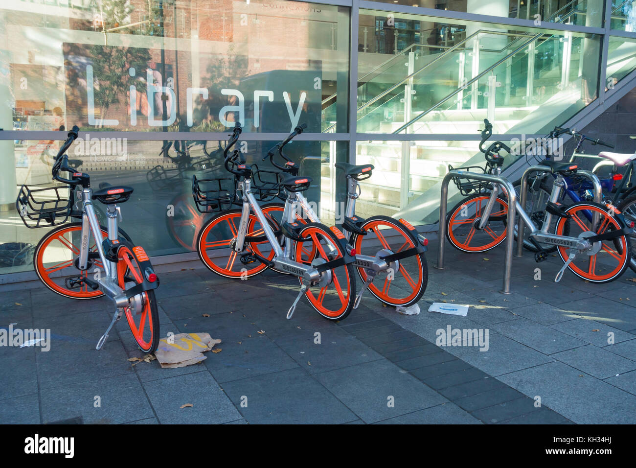 Mobikes, die für die Verwendung durch ein Handy app gemietet werden kann ein GPS-Tracker hier außerhalb der zentralen Bibliothek auf einem verunreinigt Gehweg versehen geparkt Stockfoto